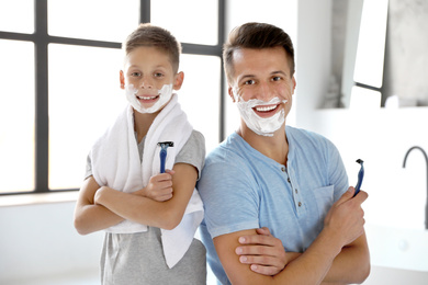 Happy father and son with shaving foam on their faces in bathroom