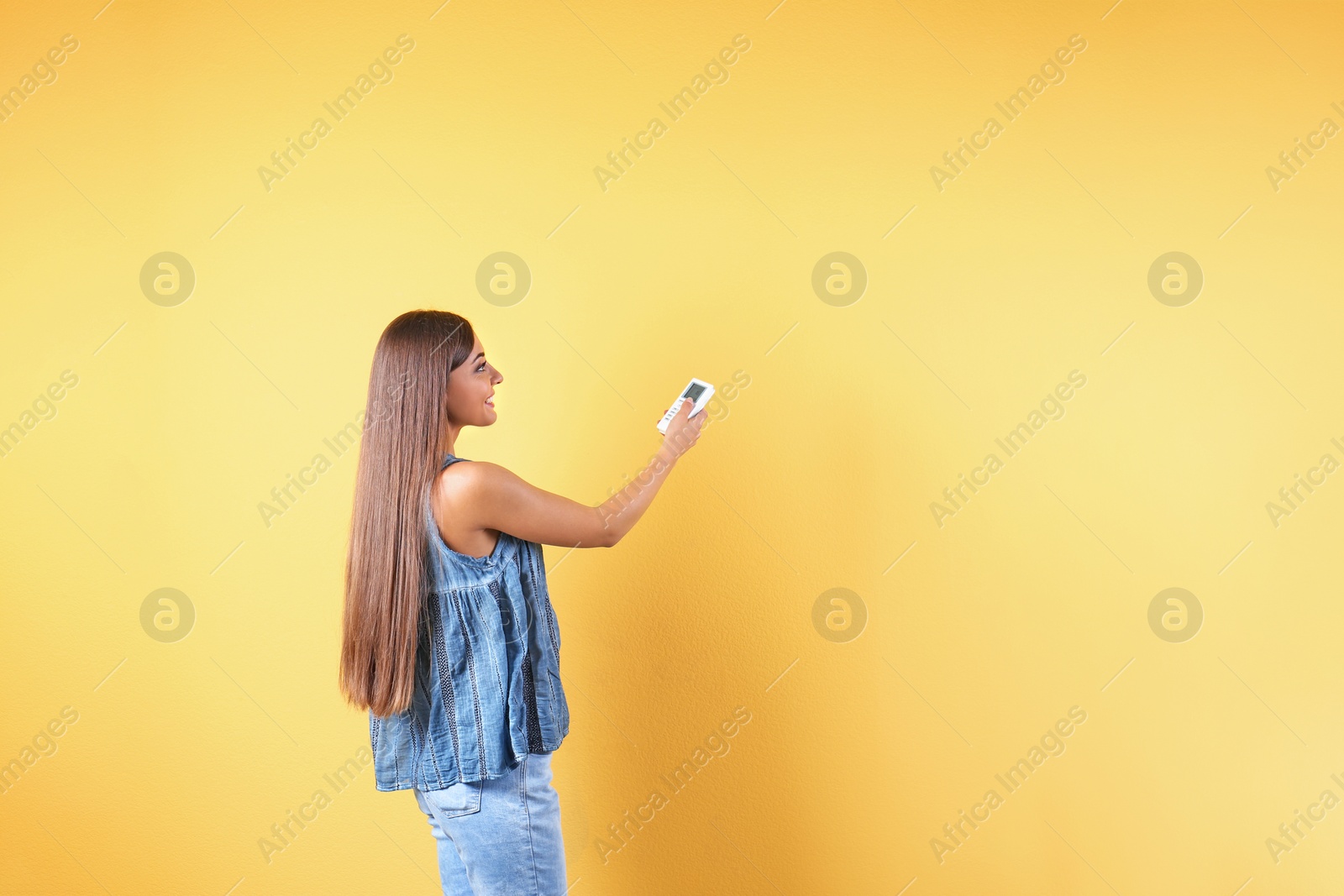 Photo of Young woman with air conditioner remote on color background, copy space text