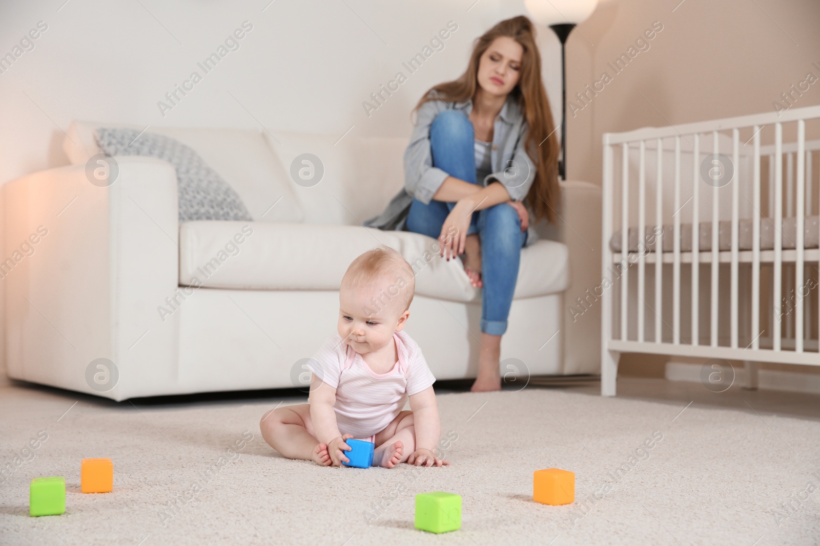 Photo of Cute baby girl playing on floor and young mother suffering from postnatal depression at home