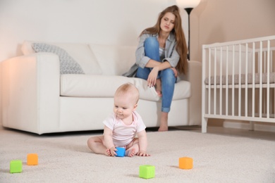 Photo of Cute baby girl playing on floor and young mother suffering from postnatal depression at home