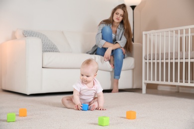 Cute baby girl playing on floor and young mother suffering from postnatal depression at home