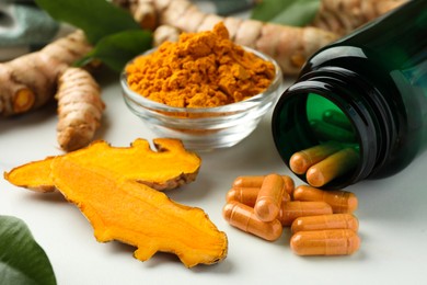 Photo of Turmeric roots, pills and powder on white table, closeup