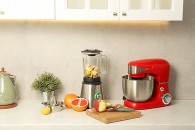 Photo of Modern red stand mixer, blender, artificial plant and different ingredients on white marble countertop in kitchen