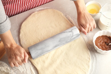 Woman rolling dough for cinnamon rolls on table, closeup