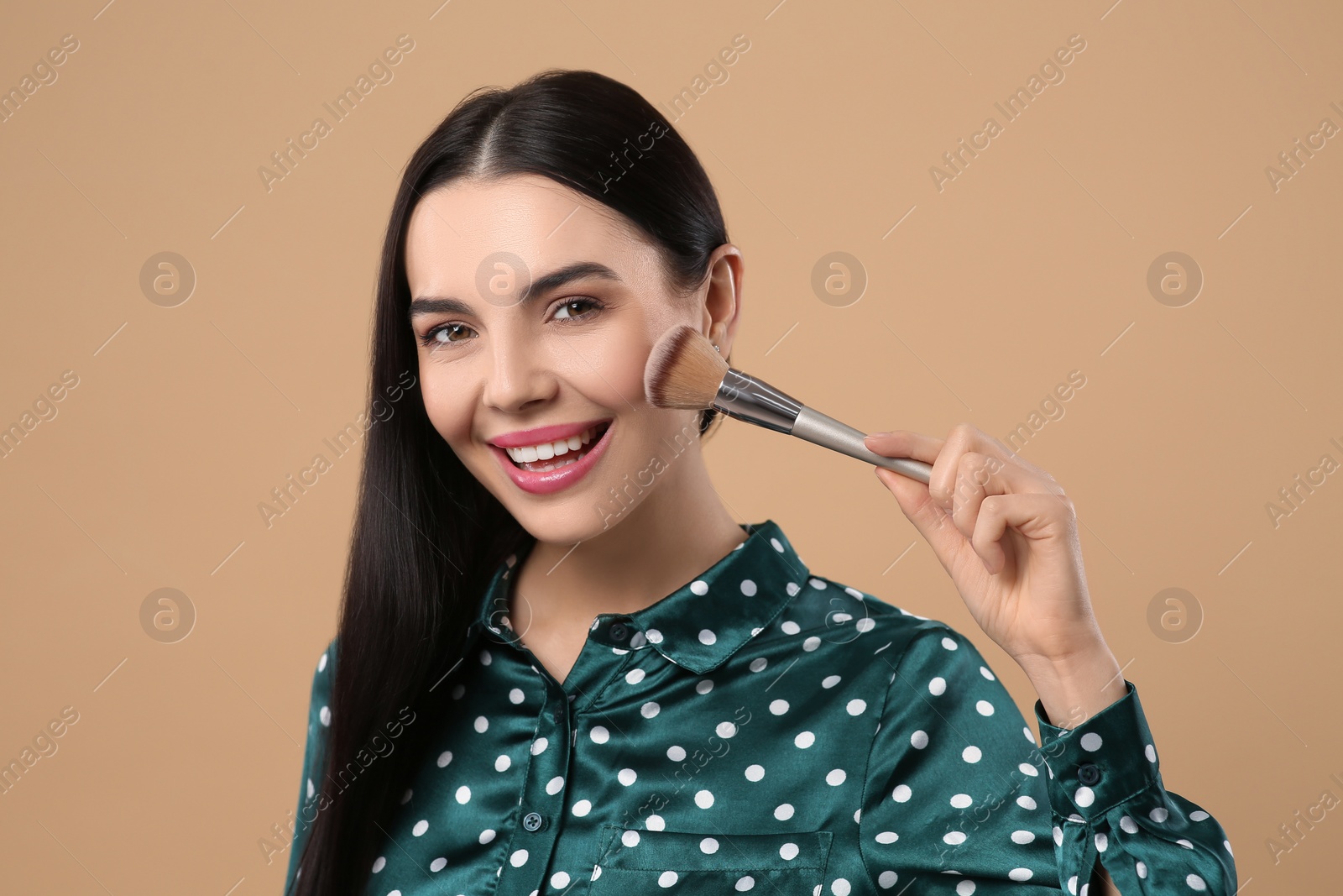 Photo of Happy woman with makeup brush on light brown background