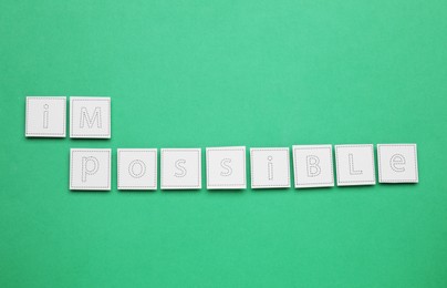 Photo of Motivation concept. Changing word from Impossible into Possible by removing paper with letters I and M on green background, top view