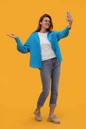 Photo of Beautiful woman in eyeglasses taking selfie on orange background