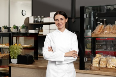 Photo of Portrait of happy baker near showcase with pastries in her cafe