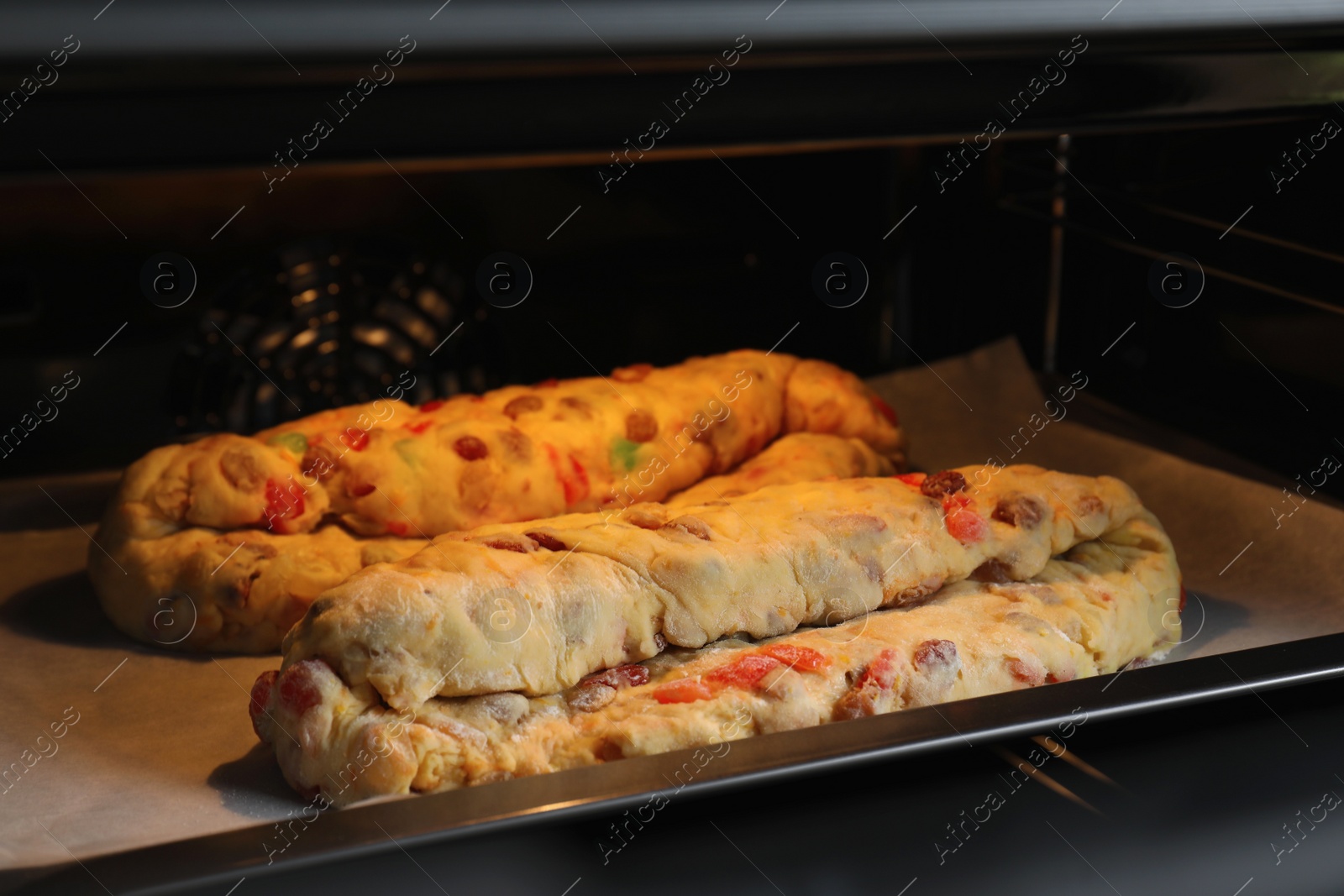 Photo of Raw homemade Stollens with candied fruits and nuts on baking tray in oven, closeup. Traditional German Christmas bread