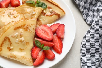 Delicious thin pancakes with strawberries, cottage cheese and honey on light table, closeup