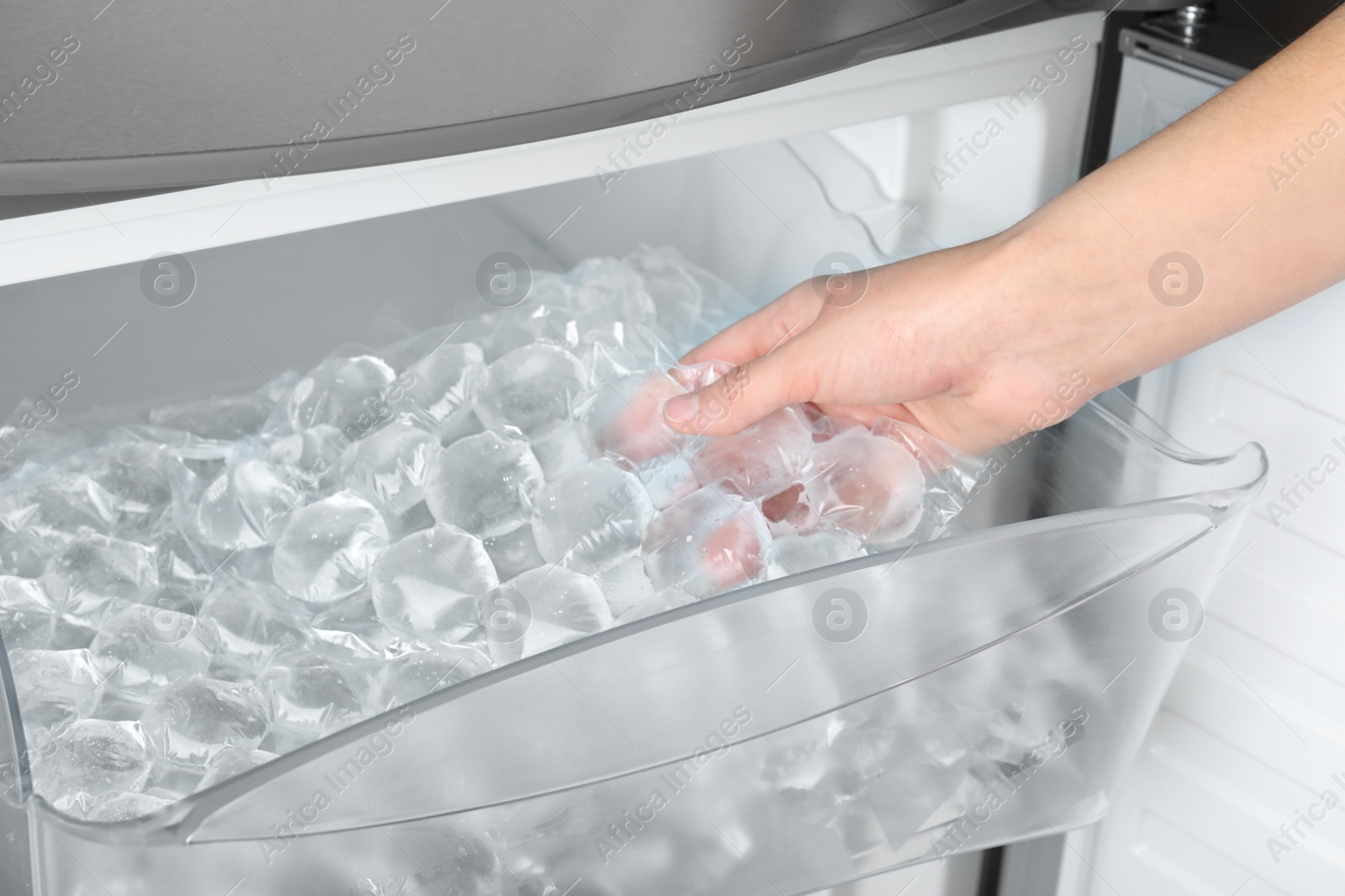 Photo of Woman taking plastic bag with ice cubes from fridge, closeup