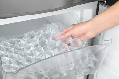 Photo of Woman taking plastic bag with ice cubes from fridge, closeup