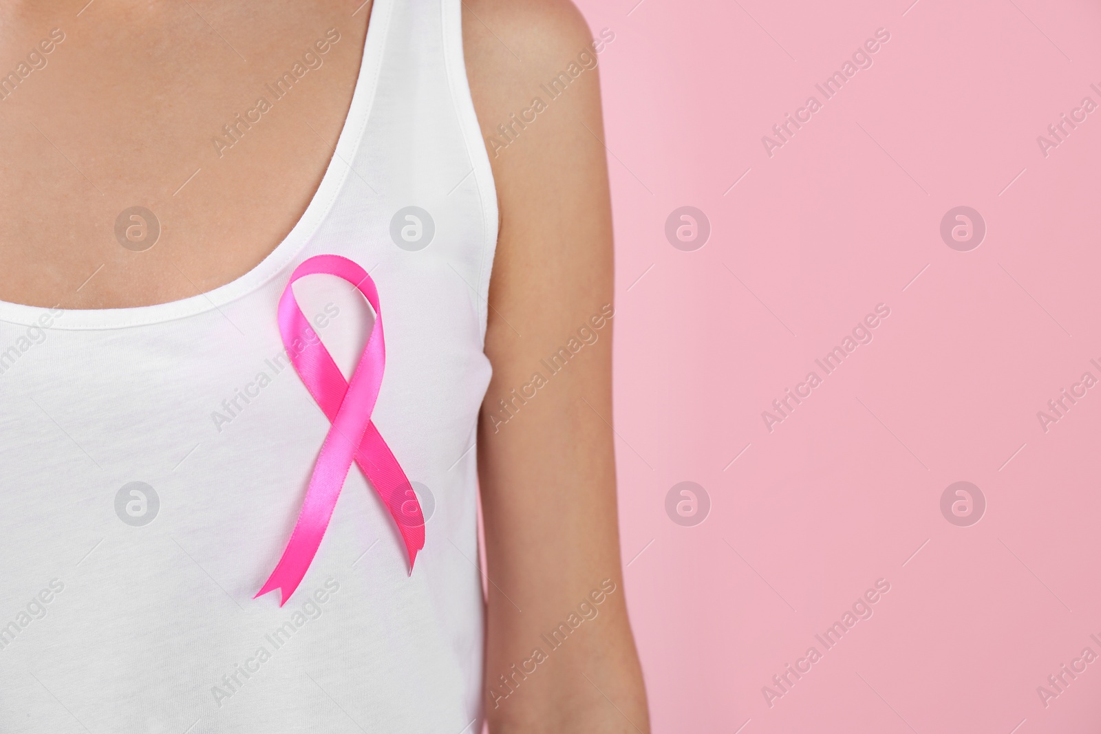 Photo of Woman with pink ribbon on color background, closeup with space for text. Breast cancer awareness