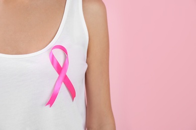 Photo of Woman with pink ribbon on color background, closeup with space for text. Breast cancer awareness