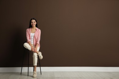 Photo of Beautiful young woman sitting on stool near brown wall. Space for text