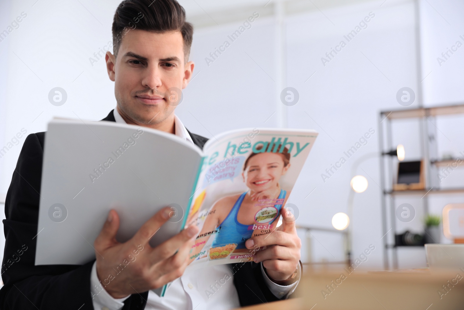 Photo of Man reading magazine at table in office