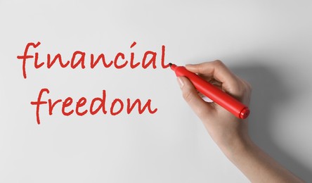 Image of Woman writing words Financial Freedom on white background, top view