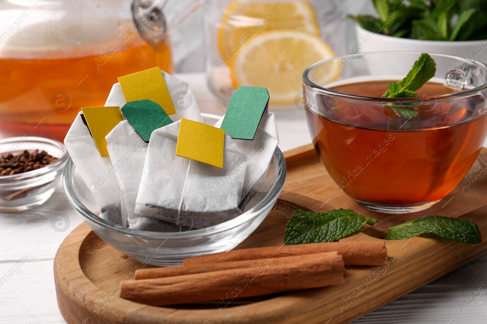 Photo of Tea bags, cup of hot drink, cinnamon sticks and mint on white wooden table, closeup