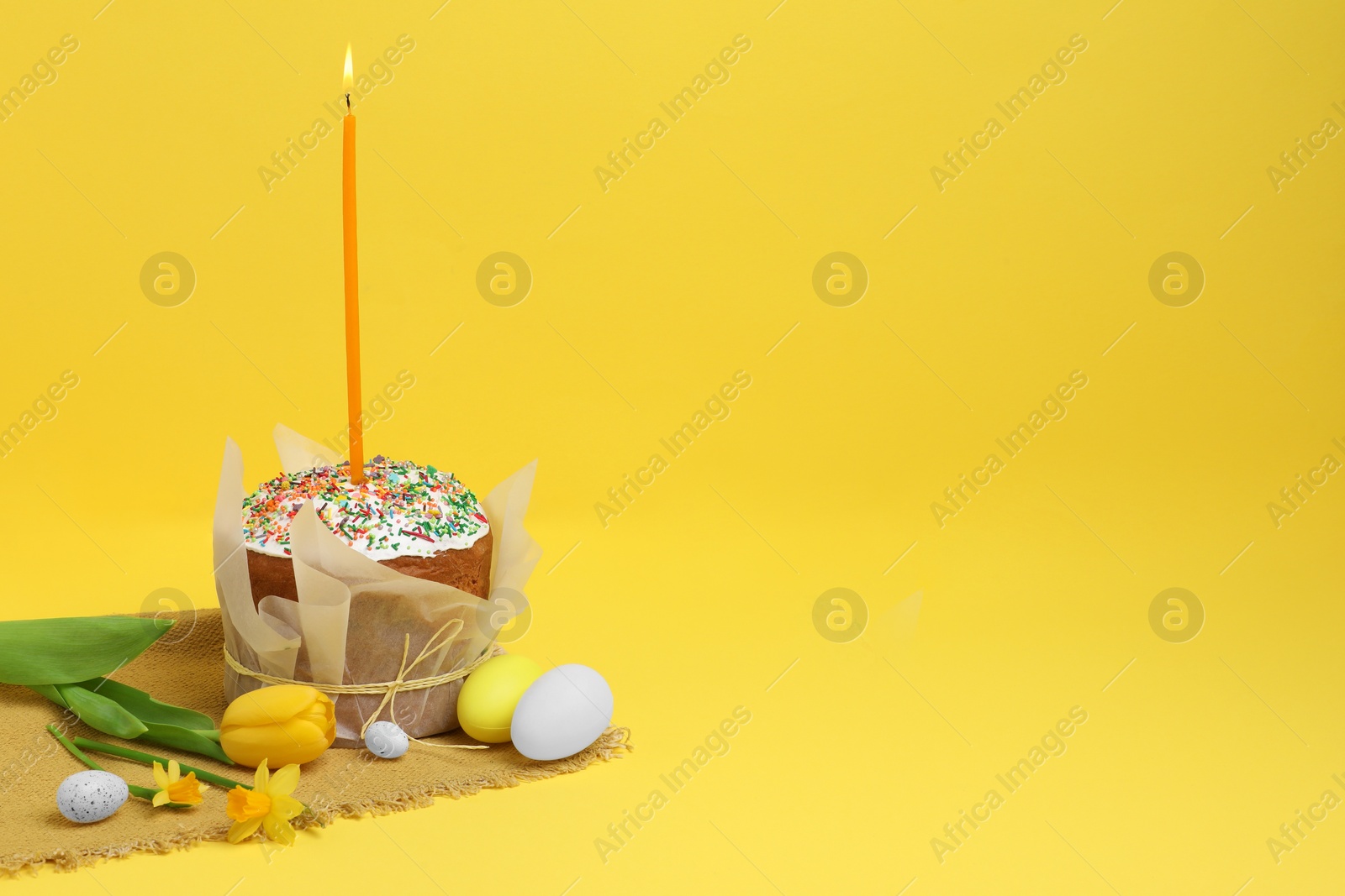 Photo of Traditional Easter cake with sprinkles, candle, decorated eggs and flowers on yellow background. Space for text