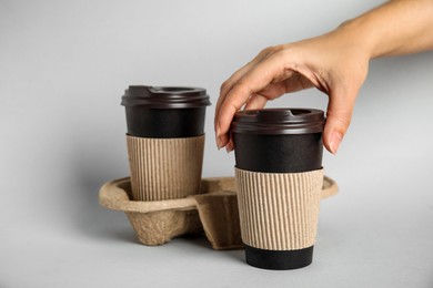 Woman taking paper coffee cup with cardboard sleeve on grey background, closeup