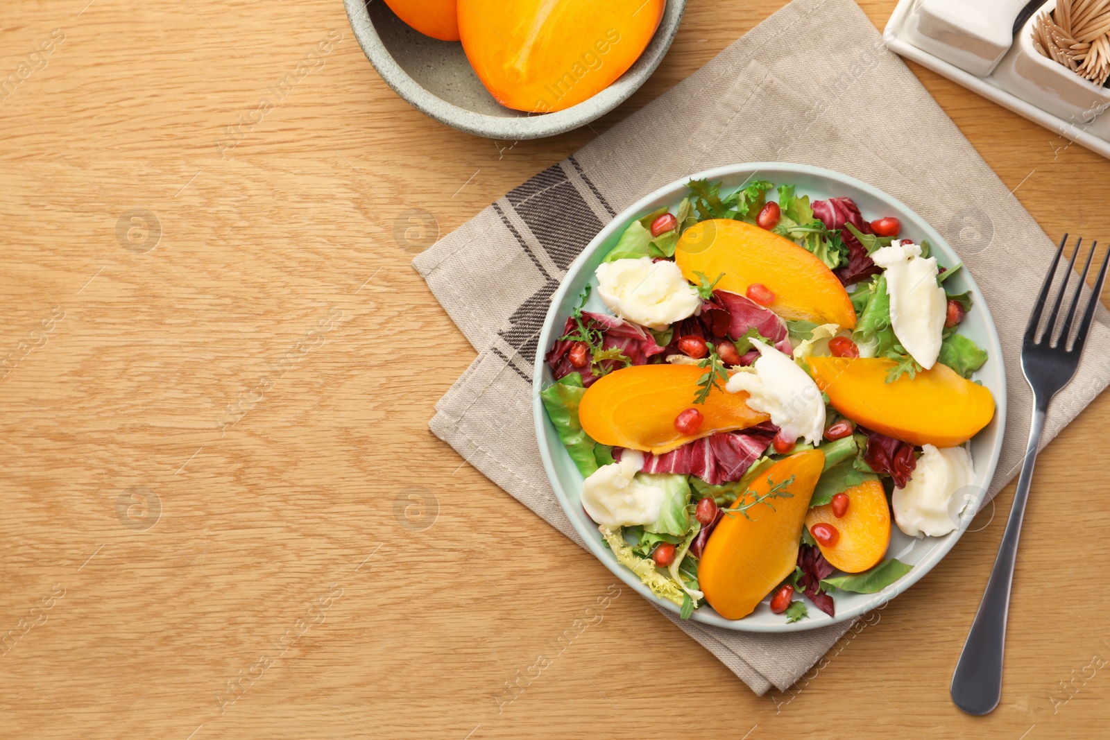 Photo of Delicious persimmon salad with cheese and pomegranate served on wooden table, flat lay. Space for text