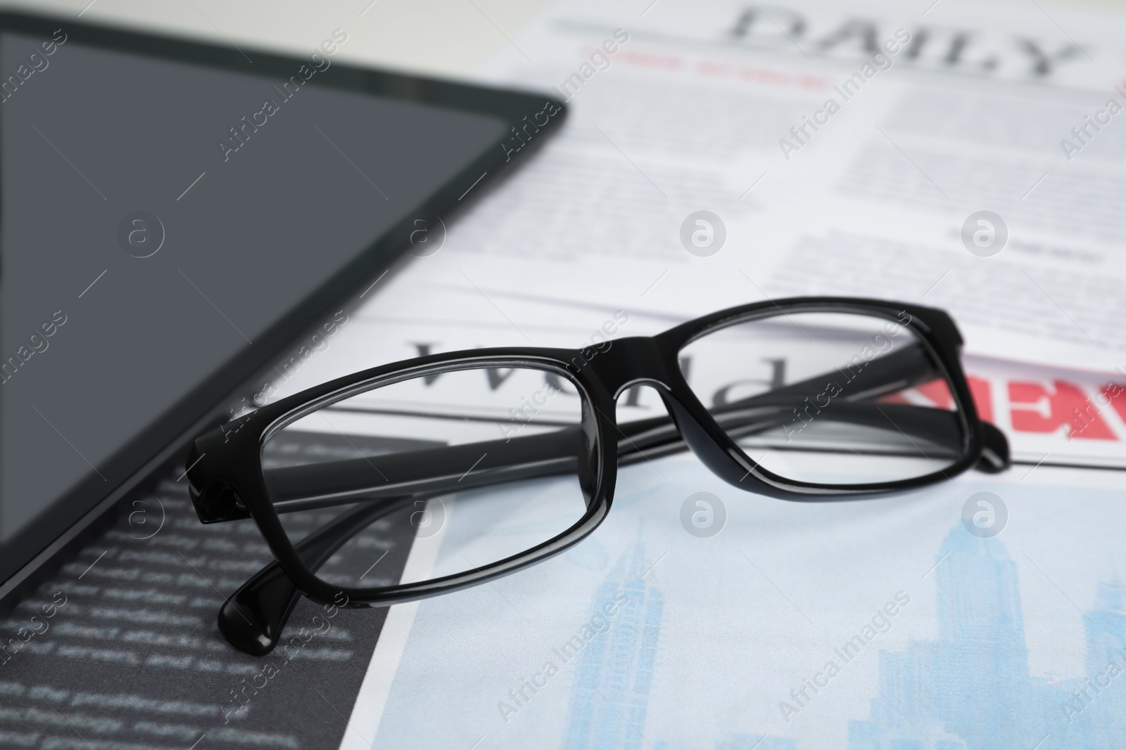 Photo of Glasses and tablet on newspaper, closeup view