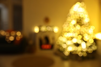 Stylish fireplace between Christmas tree and sofa in cosy room, blurred view