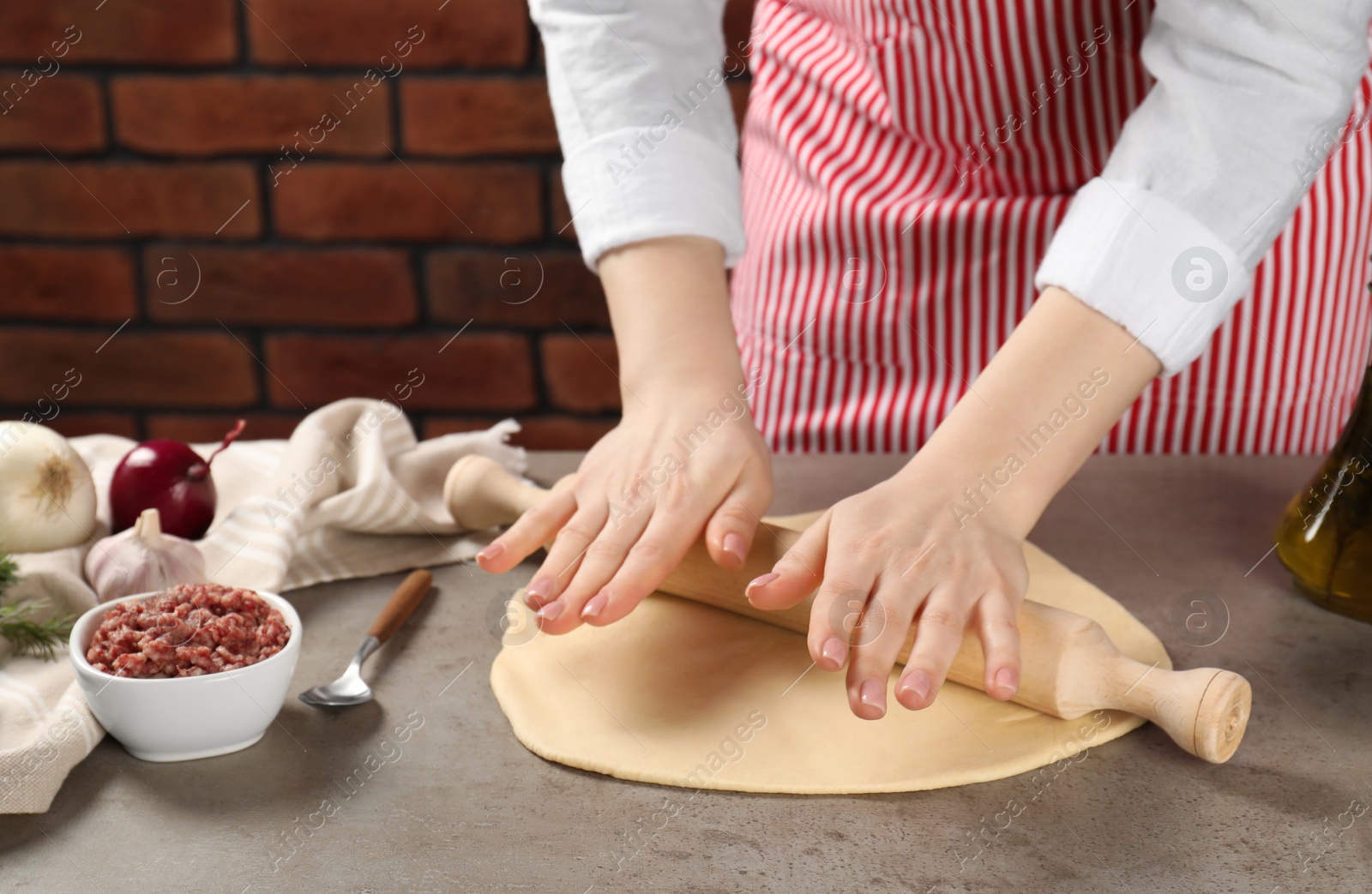 Photo of Woman rolling raw dough at grey table, closeup