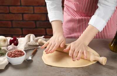 Woman rolling raw dough at grey table, closeup