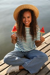 Beautiful young African American woman with pieces of watermelon on wooden pier near river