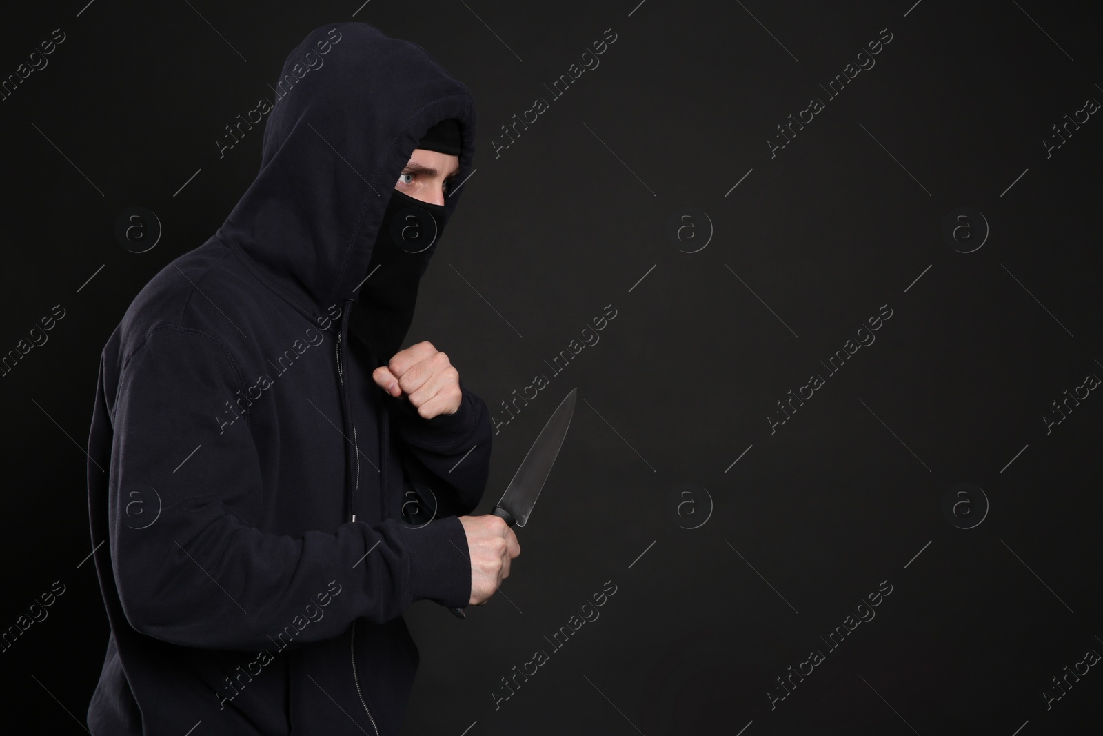 Photo of Man in mask with knife on black background, space for text. Dangerous criminal