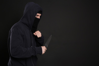 Man in mask with knife on black background, space for text. Dangerous criminal