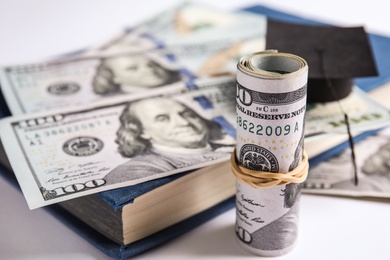 Photo of Dollar banknotes, mini student graduation hat and book on white background. Tuition fees concept