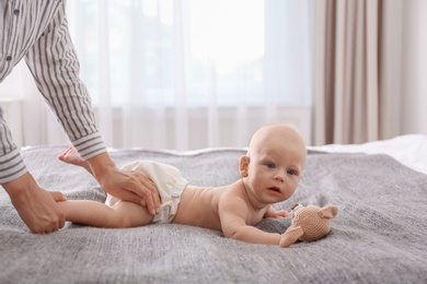Photo of Young woman massaging cute little baby on bed at home