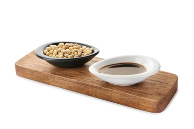 Wooden board with dishes of soy sauce and beans on white background