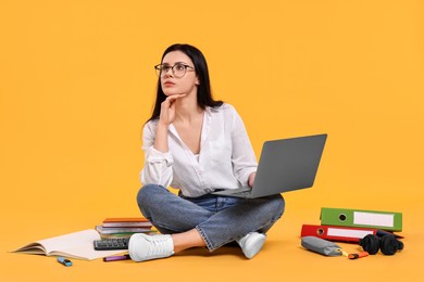 Student with laptop sitting among books and stationery on yellow background