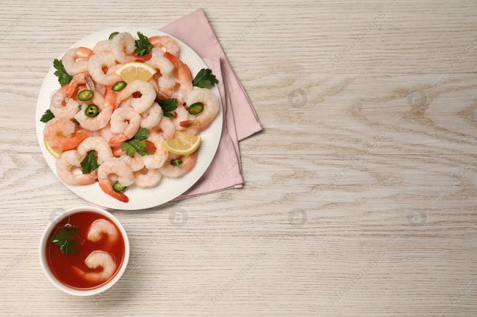 Photo of Tasty boiled shrimps with cocktail sauce, chili, parsley and lemon on light wooden table, flat lay. Space for text