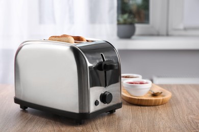 Toaster with roasted bread and jam on wooden table, space for text