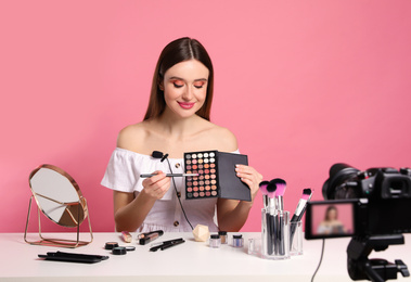Beauty blogger recording makeup tutorial on pink background