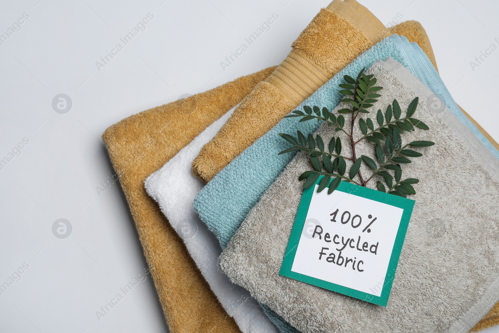 Photo of Recycling concept. Stacked towels and card with plant on white background, top view
