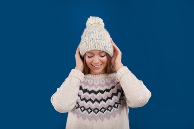 Photo of Young woman in warm sweater and hat on blue background. Winter season