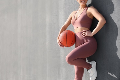 Young woman in stylish sports wear holding ball on grey background, closeup. Space for text