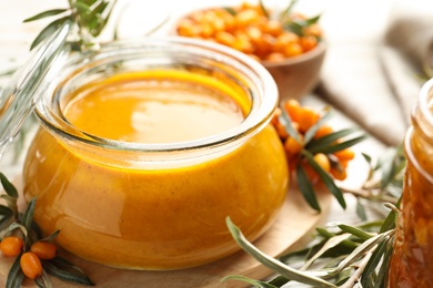 Photo of Delicious sea buckthorn jam and fresh berries on table, closeup