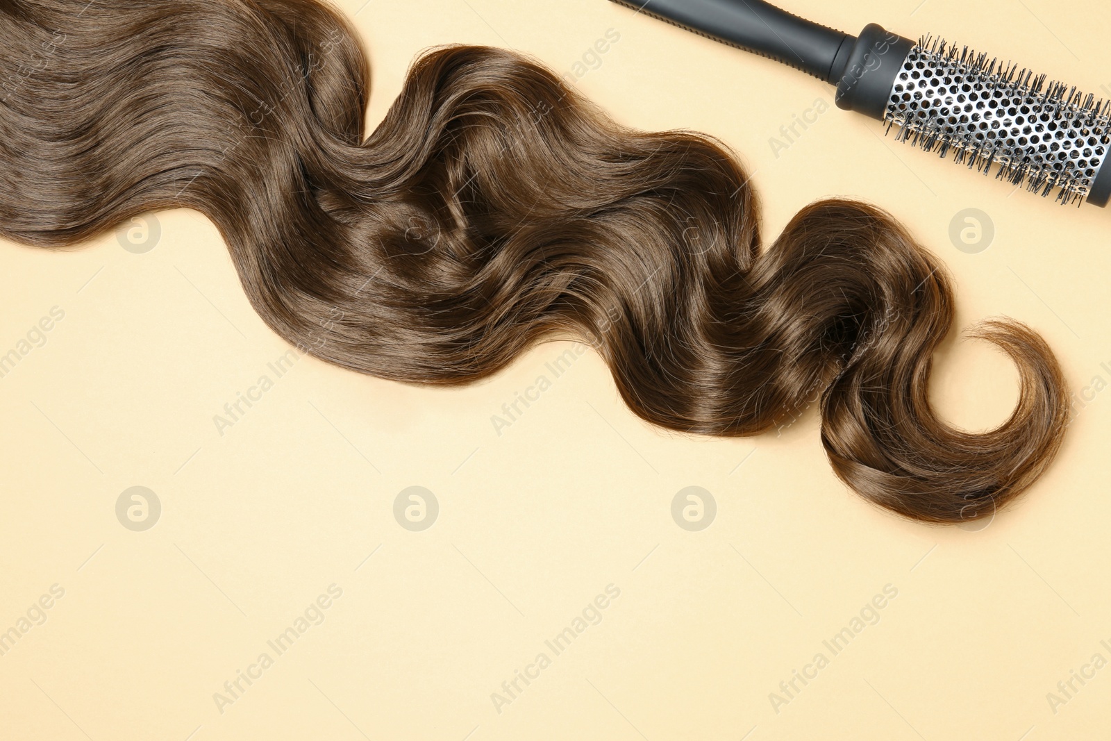 Photo of Lock of brown wavy hair and brush on color background, flat lay. Space for text