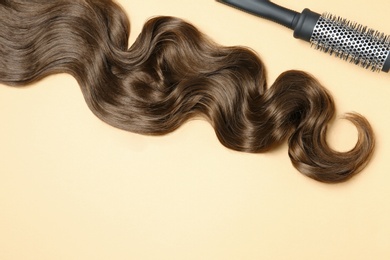 Lock of brown wavy hair and brush on color background, flat lay. Space for text