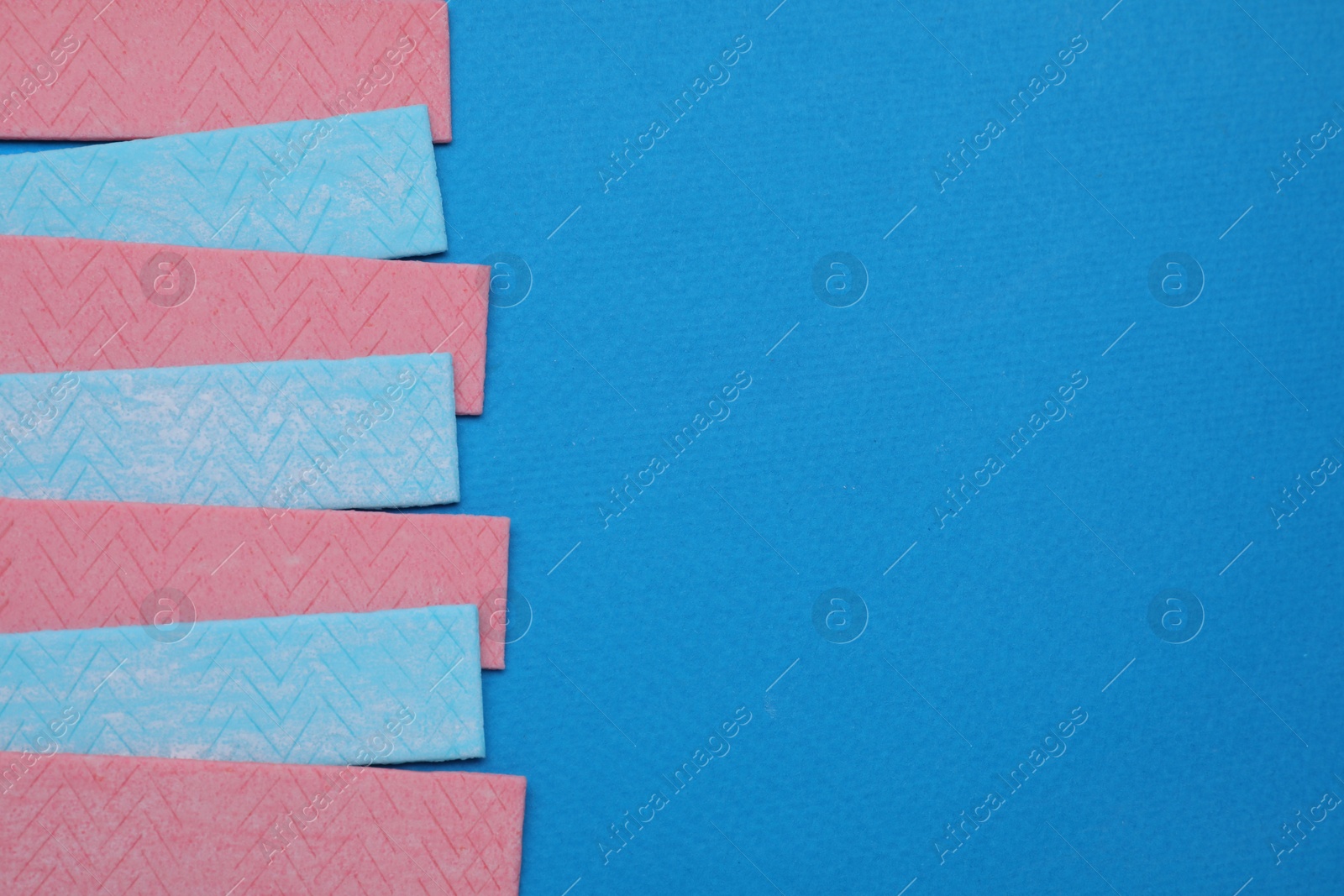 Photo of Many sticks of tasty chewing gum on light blue background, flat lay. Space for text