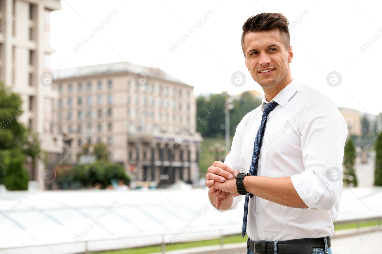 Photo of Portrait of handsome young man checking time on city street. Space for text