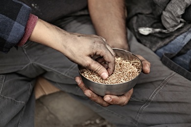 Poor homeless people with bowl of wheat outdoors, closeup