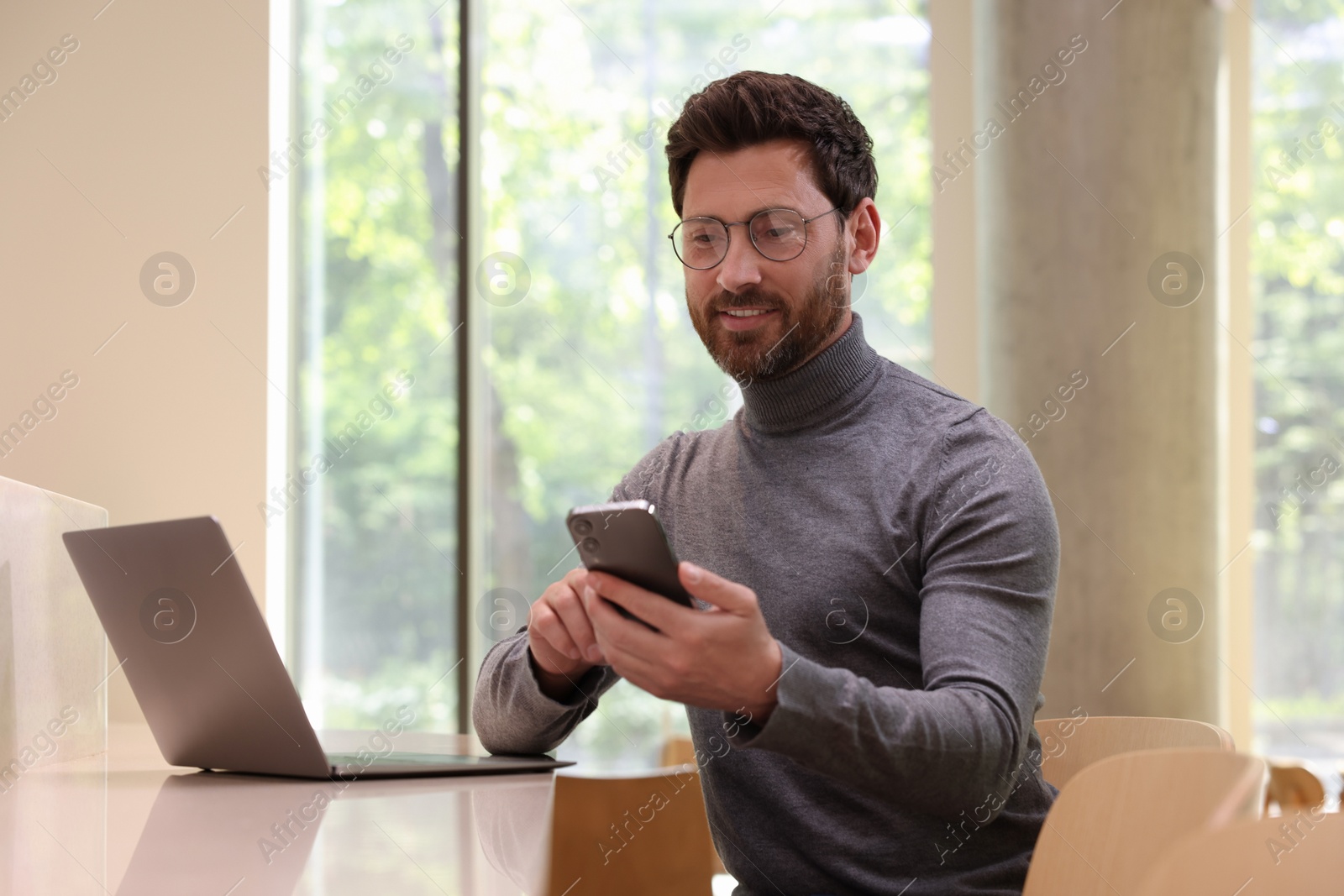 Photo of Handsome man sending message via smartphone at table indoors