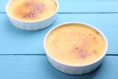 Photo of Delicious creme brulee in bowls on light blue wooden table, closeup